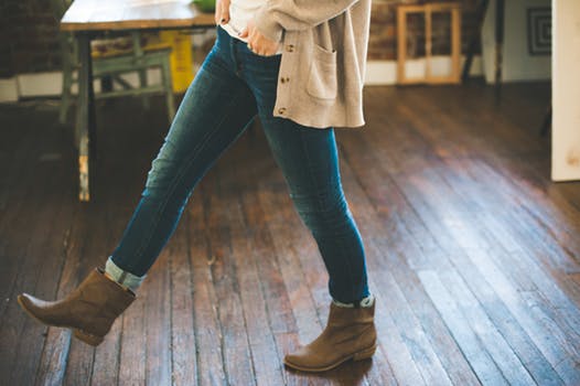 Girl in blue jeans wears brown boots with studs as she walks across a wooden floor.